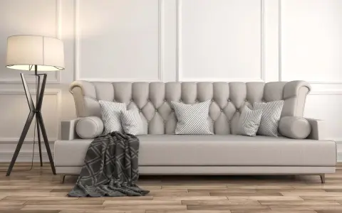 Divano imbottito grigio con cuscini a righe e coperta geometrica. La luce soffusa di una lampada da terra illumina la scena, dimostrando come grigio e beige stiano bene insieme.