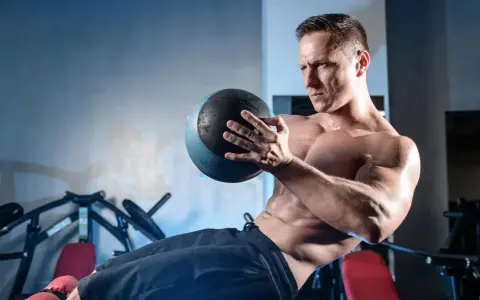 Un homme transpire en faisant un exercice oblique avec un ballon de médecine dans une salle de sport.