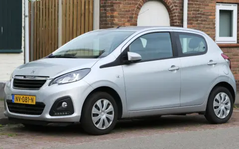Srebrny Peugeot 108 stoi zaparkowany przed ceglanym domem.