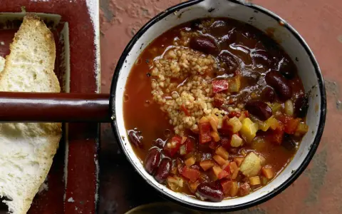 Herzhaftes Chili sin Carne mit Kidneybohnen, Bulgur und Gemüse in einem Topf, daneben geröstetes Brot.