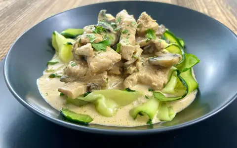 Pyszny keto obiad z kurczakiem w kremowym sosie z pieczarkami, podany z makaronem z cukinii.