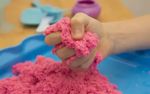 Kind hält pinken kinetischen Sand, der sich leicht formen lässt. Perfekt zum **kinetic sand selber machen** und Spielen.