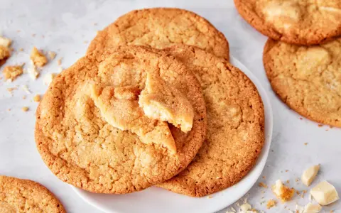 Saftige white chocolate cookies, eine davon angebrochen, mit Stückchen weißer Schokolade und Krümeln daneben.