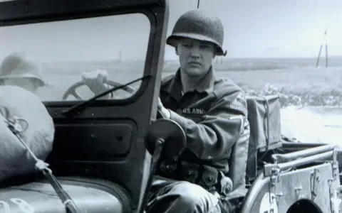 Elvis Presley in seiner US Army Uniform, sitzt am Steuer eines Jeeps.
