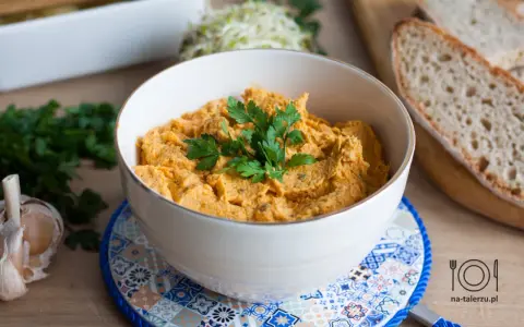 Pyszna pasta z kurczaka w miseczce, udekorowana natką pietruszki, obok czosnek i kromki chleba.