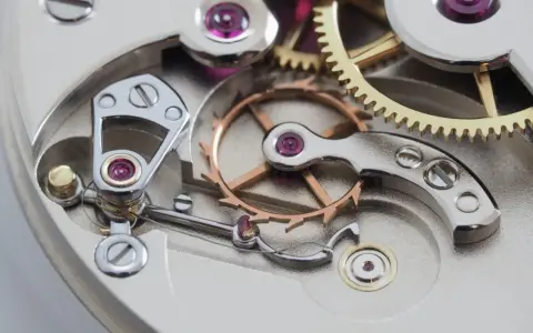 Meccanismo di orologio con ingranaggi dorati e ruota bilanciere, parte di uno scappamento coassiale.