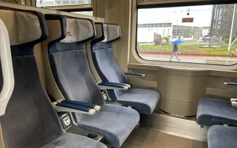 Wygodne siedzenia w wagonie z przedziałami Intercity 2 klasa. Za oknem deszczowa pogoda i przechodzień z niebieskim parasolem.