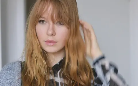 Ein junges Mädchen mit langen, welligen Haaren und Pony, das sich die Haare stylt.