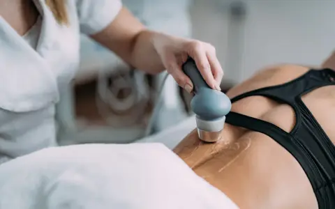 Rehabilitacja ultradźwięki na czym polega? Fizjoterapeuta wykonuje zabieg ultradźwiękami na plecach pacjentki, co pomaga w leczeniu bólu i regeneracji tkanek.