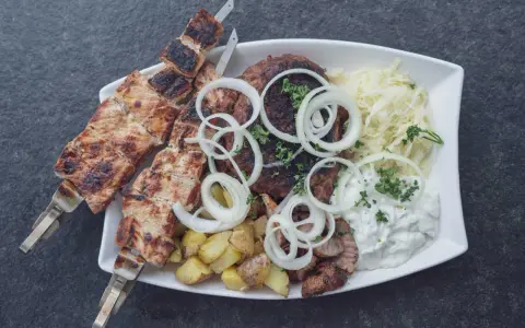 Ein Teller mit gegrilltem Fleisch, Kartoffeln und Krautsalat, garniert mit Zwiebelringen. Ein authentisches Souvlaki Rezept original.