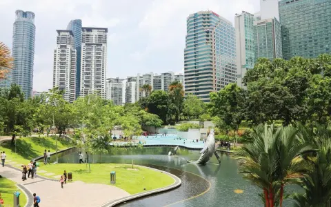 Park z rzeźbą wieloryba i basenem w stolicy Malezji, Kuala Lumpur, otoczony nowoczesnymi wieżowcami.
