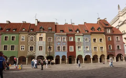 Kolorowe kamienice na Starym Rynku w Poznaniu, gdzie kwitnie rozrywka. Ludzie spacerują po bruku, podziwiając architekturę.