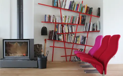 Camino acceso, attrezzi da camino, e moderne piccole librerie rosse piene di libri, con sedie colorate.