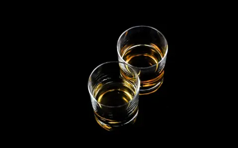 Dwa szklanki z bursztynowym płynem, idealne na wieczór z drinkiem. Czy to Baileys?