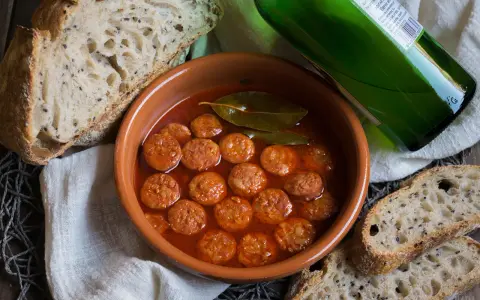 Chorizo a la sidra en cazuela de barro, acompañado de pan rústico y una botella de sidra verde.