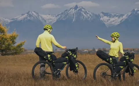 Para szykuje się na przygodę bike packing. W tle majestatyczne, ośnieżone góry.