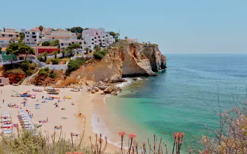 Sonnige Küste Portugals mit weißem Strand, türkisfarbenem Meer und Häusern auf den Klippen. Perfekt für eine Portugal Wetter Jahresübersicht.