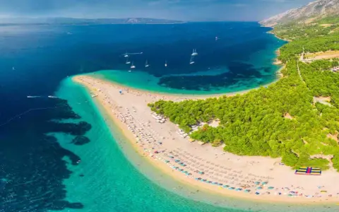 Plaża w kształcie języka, otoczona turkusową wodą i zielonym lasem, z widokiem na góry.