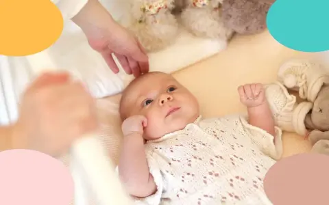 Un bebé despierto en su cuna, con una mano acariciándole la cabeza. Parece que mi bebe tarda mucho en dormirse.
