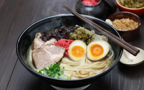 Pyszny ramen co to? Aromatyczny bulion, makaron, plastry wieprzowiny, jajko na pół, szczypiorek i marynowane dodatki.