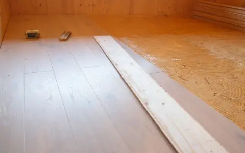 Holzboden wird verlegt. OSB-Platten sind mit Kleber vorbereitet, darauf werden helle Dielen verlegt.