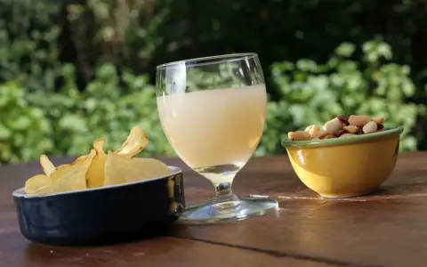 Verre de boisson claire, chips croustillantes et mélange de fruits secs, une spécialité PACA pour un apéritif ensoleillé.
