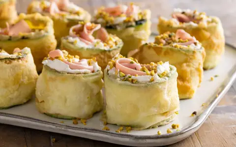 Rotolini di zucchine impanate e fritte, farciti con crema, prosciutto e pistacchi. Stuzzichini veloci ed economici perfetti per un aperitivo sfizioso.