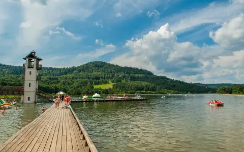 Słoneczny dzień nad zalewem Stara Morawa. Ludzie kąpią się, pływają na rowerach wodnych i odpoczywają na pomoście.