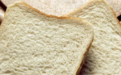 Zwei Scheiben Weißbrot liegen auf einem Holzbrett. Die Frage "wie viel Kalorien hat eine Scheibe Toast?" beschäftigt viele.