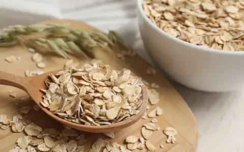 Płatki owsiane na drewnianej łyżce i w misce. Czy płatki owsiane mają gluten? Czysty owies jest bezglutenowy, ale warto sprawdzić etykietę.