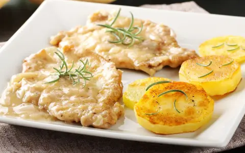 Two breaded chicken cutlets in creamy sauce with rosemary, served with pan-fried potato slices.