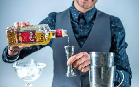 Barman nalewa Olmeca Tequila Gold do jiggera, idealna tequila do margarity. Obok kieliszek z lodem i shaker.