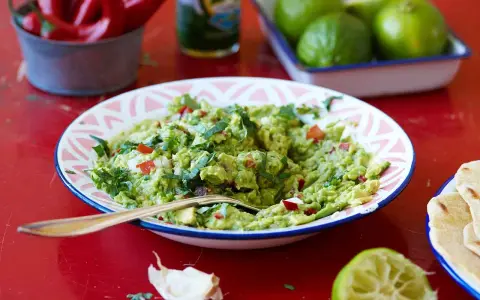En skål med krämig guacamole, perfekt för ditt nästa guacamole recept. Serveras med tortillabröd, lime och chili.