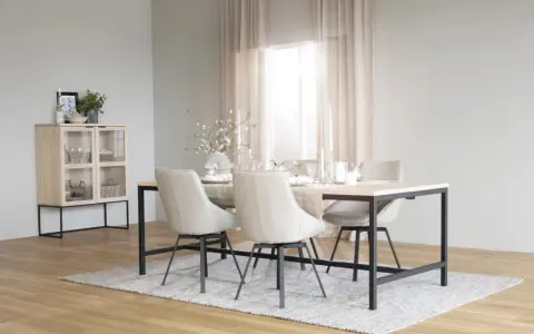 Ett ljust och luftigt rum med matbord och stolar i nordisk design. Ett vitrinskåp i trä och metall står till vänster.