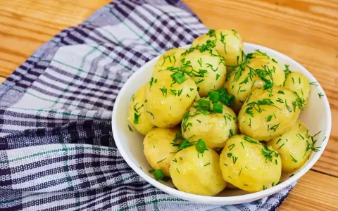 Młode ziemniaki w misce, posypane koperkiem i szczypiorkiem. Idealne na lato, a ile gotować młode ziemniaki? Krótko!