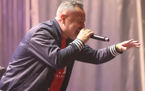 Juan Magán cantando en un escenario con micrófono y gesto animado.