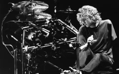 Def Leppard trummis Rick Allen sitter vid sitt trumset, redo att leverera en kraftfull rytm.