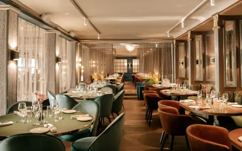 Elegant dining room at Hasselbacken restaurang, Stockholm. Tables set with glassware and cutlery, plush seating, and soft lighting create a sophisticated atmosphere.