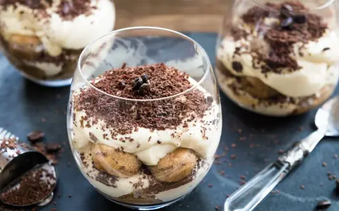 Pyszne tiramisu bez pieczenia w szklankach, udekorowane startą czekoladą i ziarnami kawy. Idealne na deser.