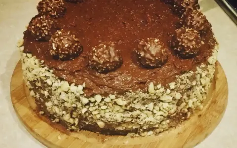 Pyszny tort ferrero rocher, oblany czekoladą i ozdobiony orzechami oraz kulkami.