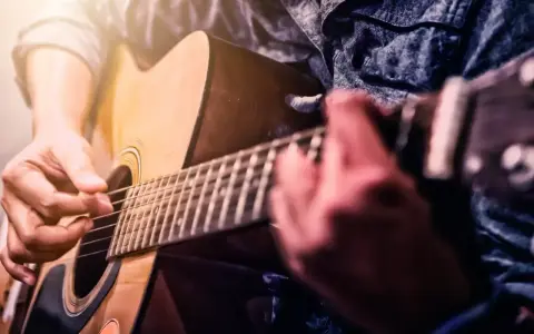 Ręce grające na gitarze akustycznej. Idealne dla tych, którzy zaczynają swoją przygodę z nauką gry na gitarze dla początkujących.