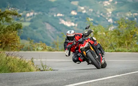 Un motociclista esperto piega in una curva stretta, con il ginocchio quasi a terra, affrontando un passo in montagna.
