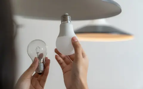 Une ampoule sans électricité, une ampoule LED moderne et une main tenant les deux, prête à remplacer l'ancienne.