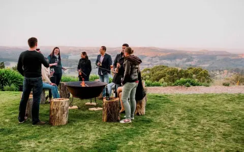 Staff retreat ideas for nonprofits: A group enjoys a bonfire and drinks outdoors, surrounded by rolling hills.