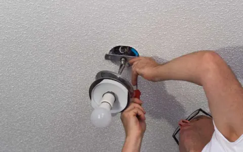 Un homme installe un luminaire au plafond avec un tournevis.