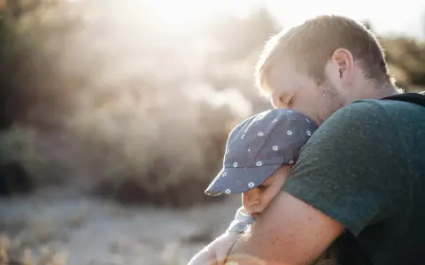 Ojciec mocno tuli dziecko w czapce z kwiatkami. To piękny moment, który pokazuje, jak ważny jest **asperger przytulanie** dla budowania więzi i poczucia bezpieczeństwa.