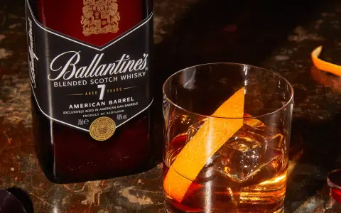 Orzeźwiający drink: whisky z wodą gazowaną, lodem i skórką pomarańczy, obok butelka Ballantine's.