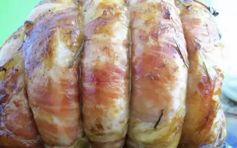 Un délicieux roti de veau, enveloppé de lard et parsemé de romarin, prêt à être dégusté.