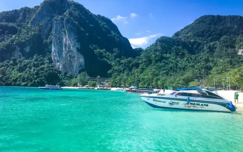 Turkusowa woda i łodzie motorowe przy plaży w Maya Bay. W tle zielone, skaliste góry.