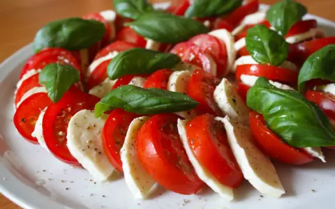 Kolorowe pomidory z mozzarellą i listkami bazylii, doprawione pieprzem, tworzą apetyczną sałatkę Caprese.